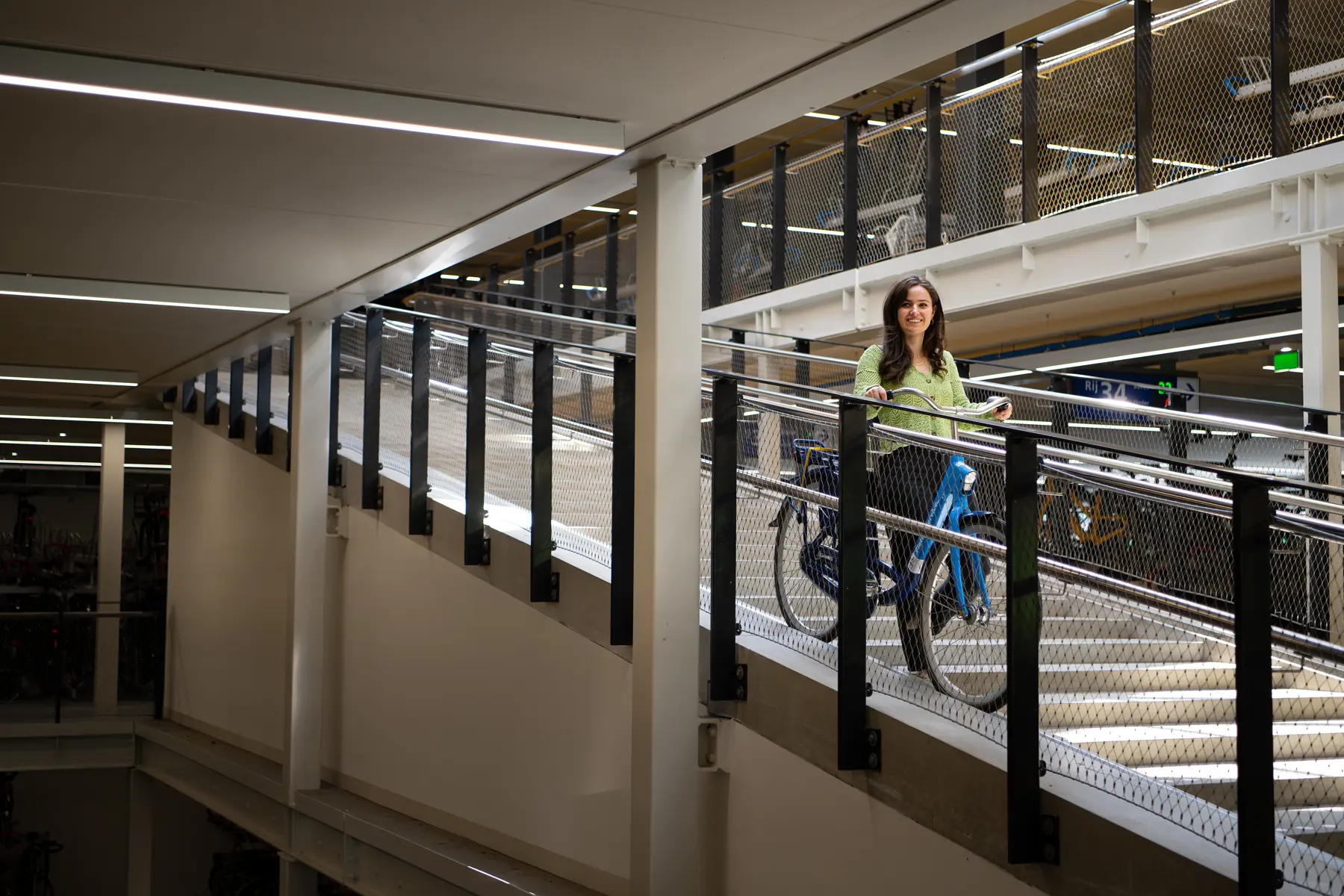 Yasmin staat in een fietsenstalling met haar fiets in haar rechterhand.